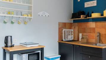 Cocina compacta con microondas, hervidor de agua, un lavamanos pequeño y estantes con cristalería y una cafetera.