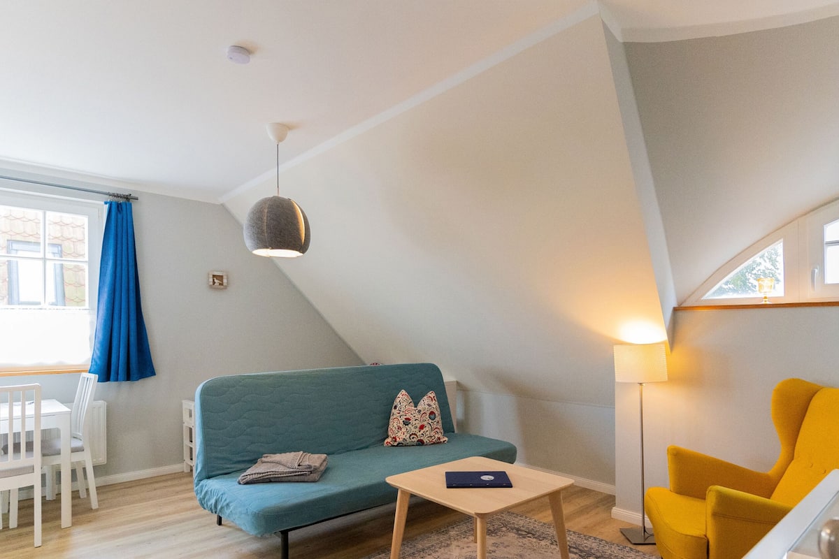 A modern living room with a teal sofa, a small wooden table, a yellow armchair, and a floor lamp.