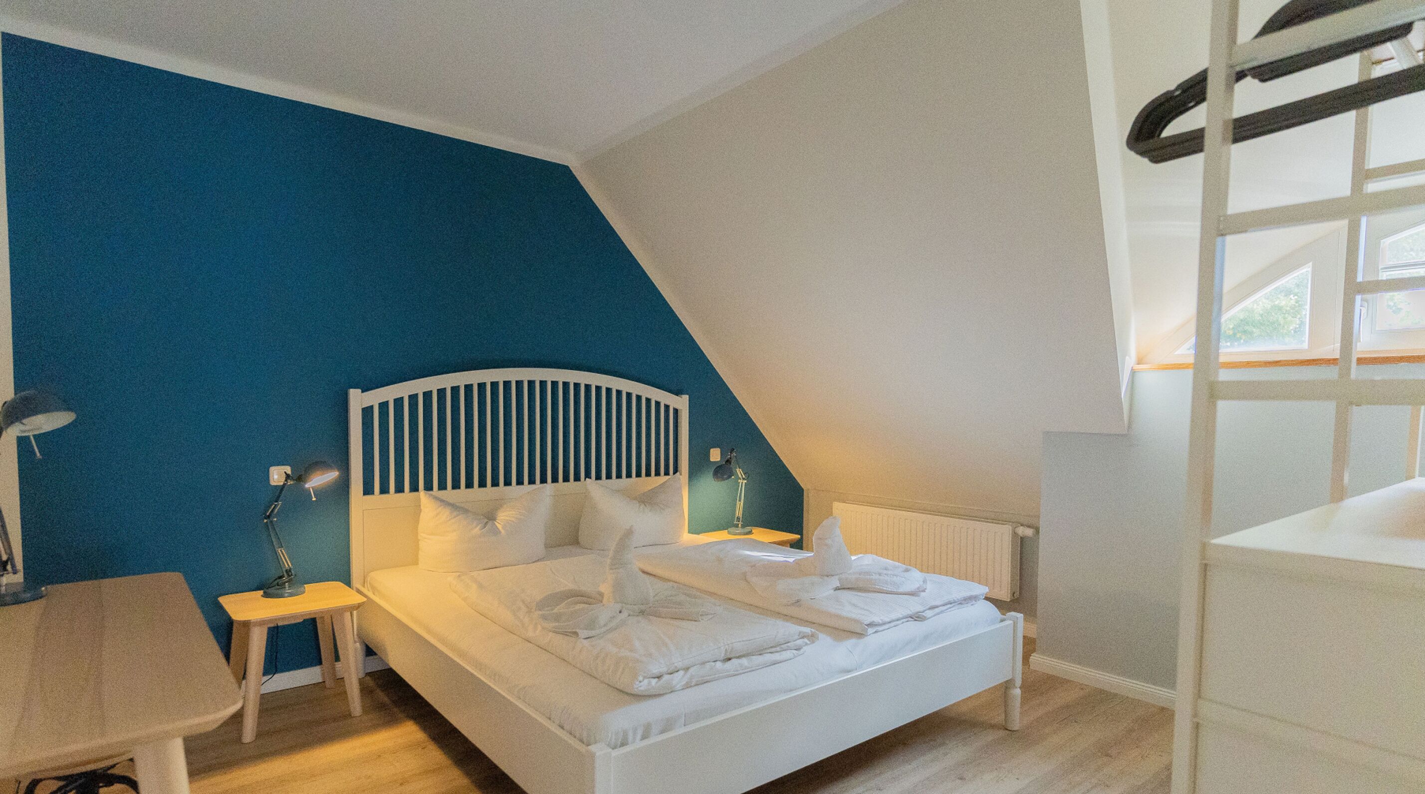 Un dormitorio con cama blanca, una mesita de noche, una lámpara y una ventana con vistas al cielo.