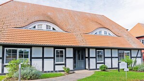 Ein traditionelles Gebäude mit Ziegeldach, mehreren Fenstern und einer kleinen Gartenanlage. Ein Schild kennzeichnet es als Mehrfamilienhaus.