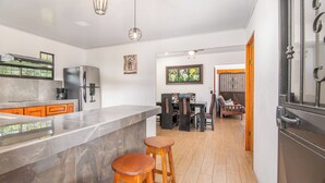 Een moderne keuken met een marmeren aanrecht, twee houten krukken en een eethoek met een tafel en stoelen.