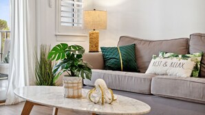 A living room with a beige sofa, a round table, a potted plant, and a lamp.