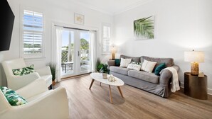 A modern living room with a grey sofa, white armchairs, a round coffee table, and a TV mounted on the wall.