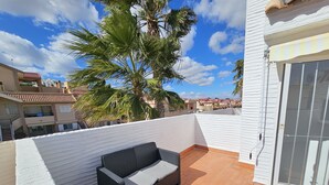 A rooftop patio with wicker furniture, a palm tree, and a view of neighboring buildings.