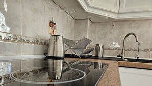 A kitchen with a modern induction cooktop, a stainless steel kettle, a toaster, and a sink with a faucet.