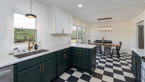 Una cocina moderna con gabinetes verde oscuro, encimeras blancas y suelo a cuadros blanco y negro.