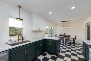 Una cocina moderna con gabinetes verde oscuro, encimeras blancas y suelo a cuadros blanco y negro.