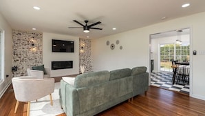 Una sala de estar moderna con un sofá verde, un sillón blanco, un televisor de pantalla plana y una chimenea.