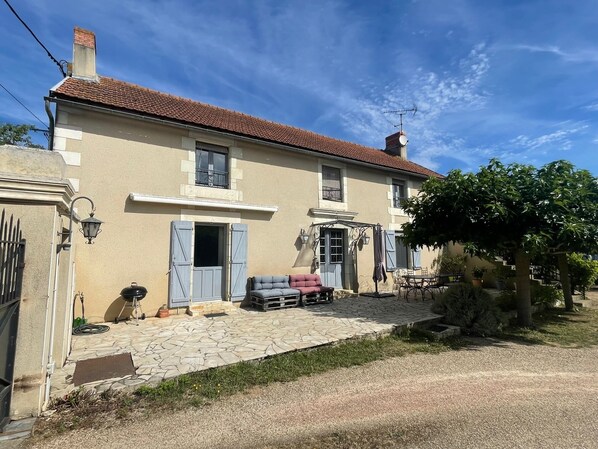 A two-story house with a tiled roof, a stone-paved patio, and a garden area with a table and chairs. - La Maison de Charlotte (Amberre)