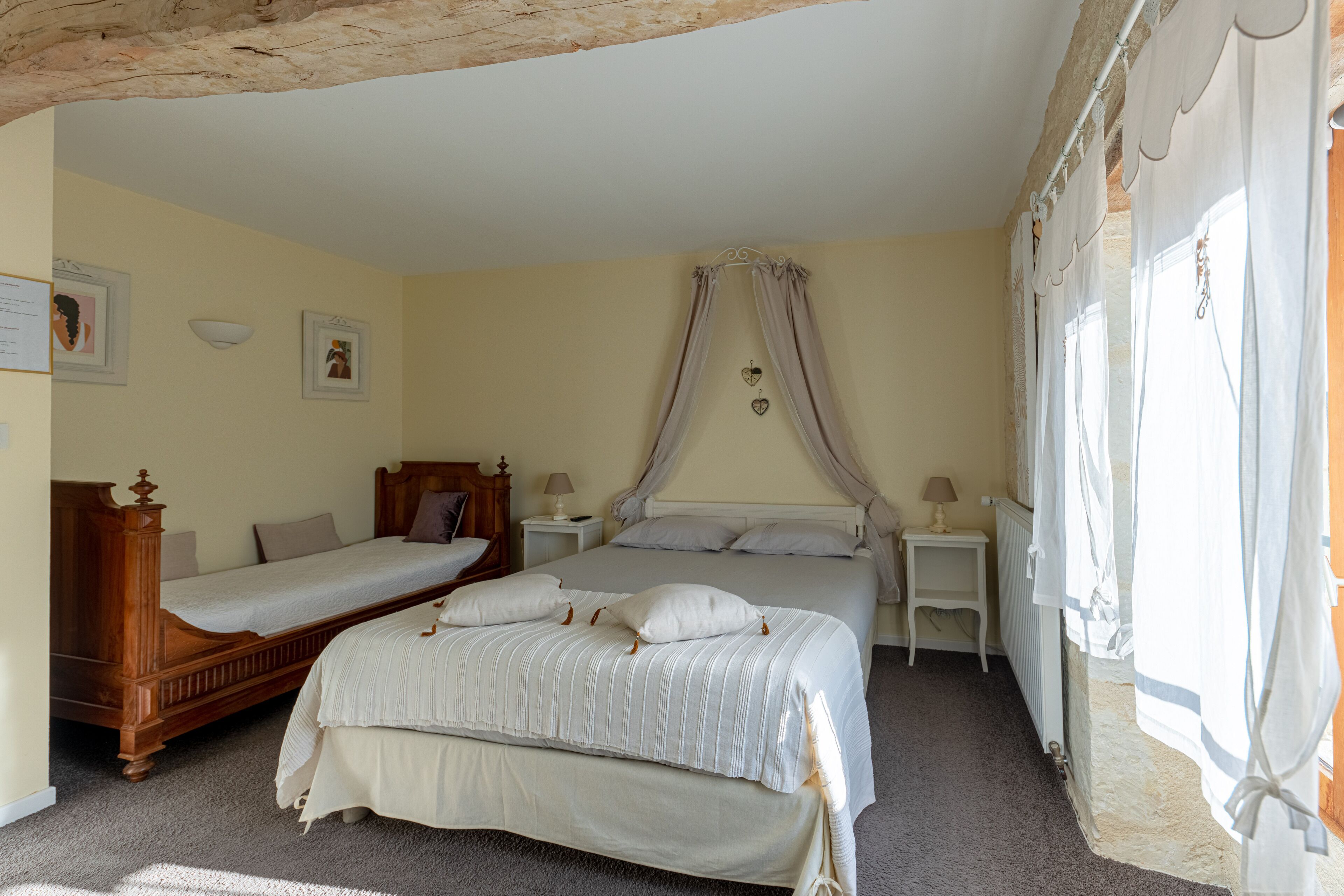 Un dormitorio con dos camas individuales, una cama con dosel, mesitas de noche con lámparas y cuadros enmarcados en la pared.
