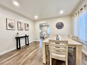 Un coin repas avec une table en bois, des chaises, une horloge et des œuvres d’art encadrées accrochées au mur.