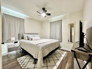 Une chambre à coucher comprenant un lit, une table de chevet, une lampe, un ventilateur de plafond et un meuble pour la télévision avec une télécommande.
