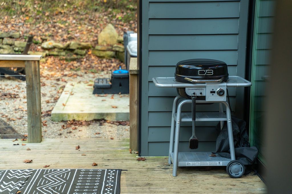 Un barbecue portable, posé sur un support métallique, se trouve à l’extérieur d’un bâtiment.