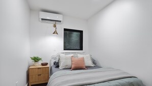 Quarto com cama, mesa de cabeceira e ar condicionado.