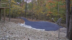 Um caminho pavimentado serpenteia por uma área arborizada, com uma estrutura de madeira à esquerda.