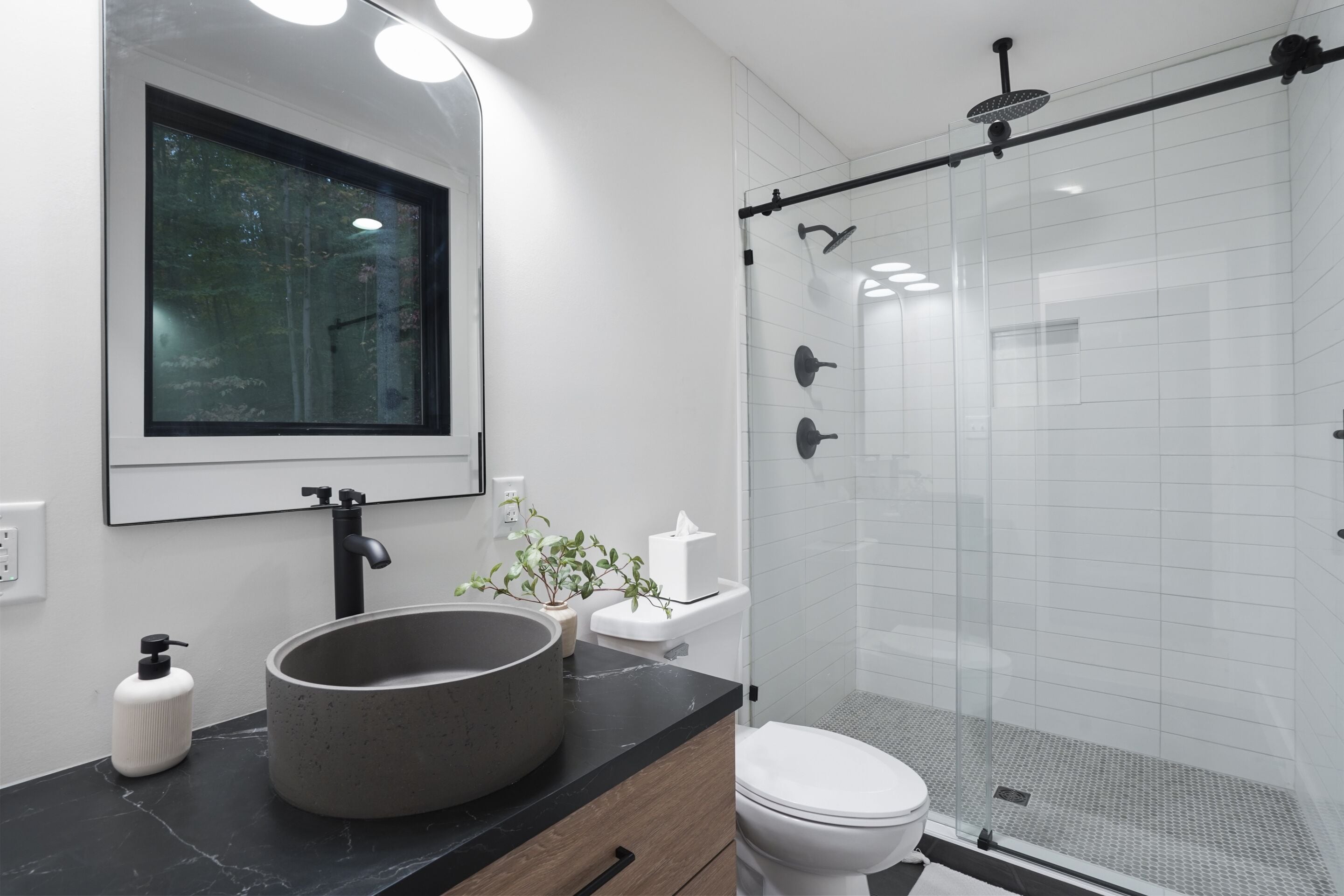 Une salle de bain moderne avec un grand lavabo rond, des toilettes et une douche séparée par une paroi de verre.