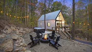 Eine Hütte mit Terrasse, Whirlpool und Feuerstelle, umgeben von Steinen.