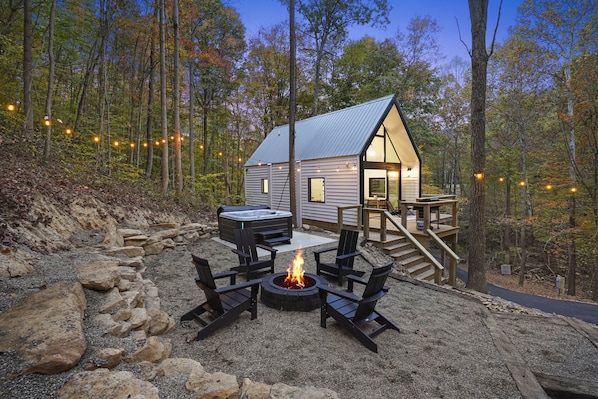 A cabin with a deck, a hot tub, and a fire pit surrounded by rocks.