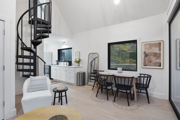 Une cuisine moderne avec des meubles blancs, un escalier en colimaçon noir et un coin repas avec des chaises noires et une table en bois.