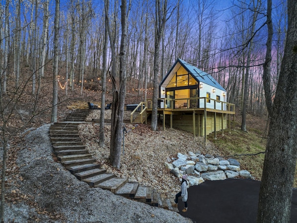 A cabin with a wooden deck, a stone pathway, and a view of the surrounding forest.