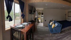 Une pièce chaleureuse avec un plafond en bois, un lit avec une literie bleue, un canapé bleu, une table à manger avec des assiettes et des verres, et une petite table avec un ventilateur et un vase.