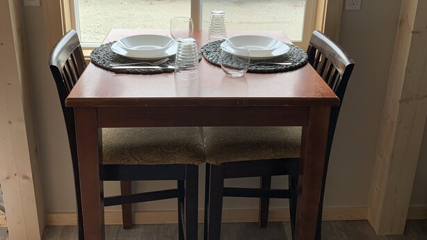 Une table à manger avec deux chaises, une fenêtre avec des rideaux et une vue sur la verdure à l’extérieur.