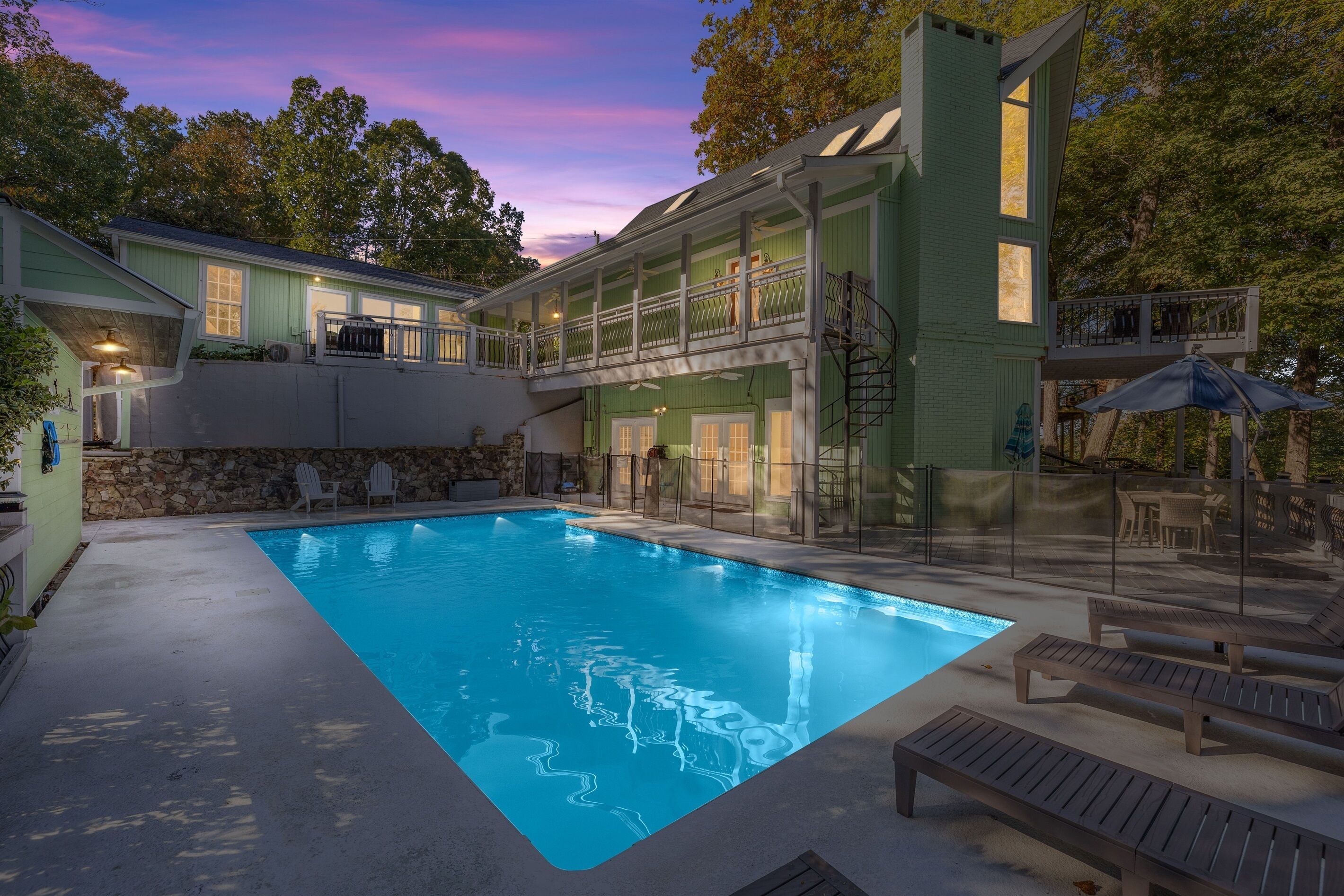 A swimming pool with a stone wall and lounge chairs, surrounded by a two-story building with a balcony.