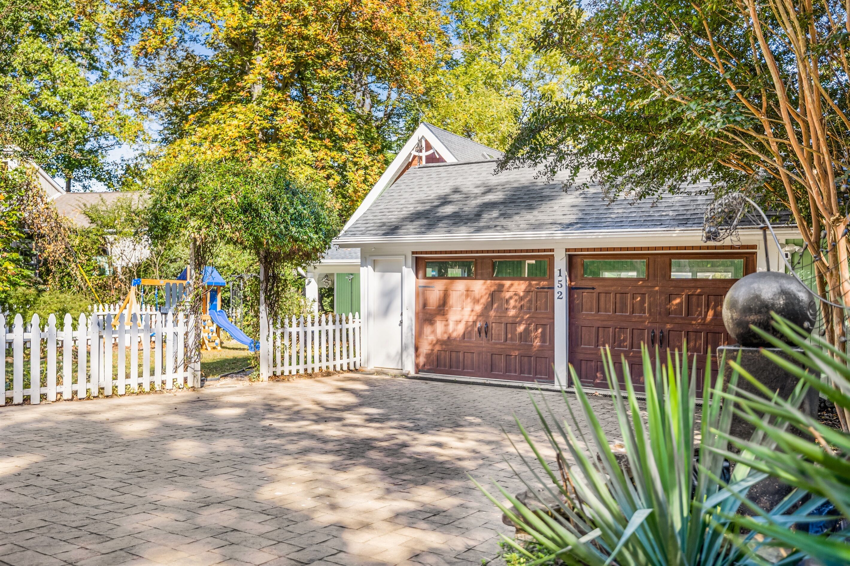 A residential garage with a brown door, a white picket fence, and a blue slide in the background.