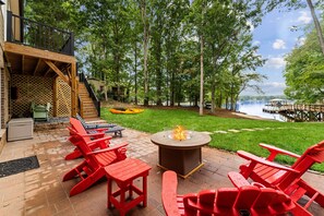 A patio with red Adirondack chairs, a fire pit, and a view of a lake with a dock. - Sandy Beach, 2 King Suites, Game Rooms & Views! (Troutman)
