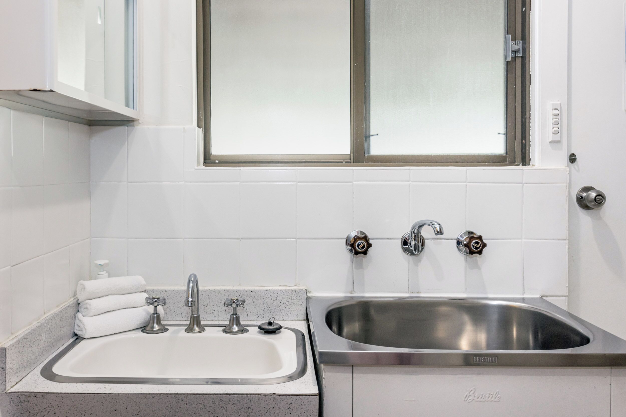 Une salle de bain avec un lavabo, deux robinets, une fenêtre et un porte-serviettes.