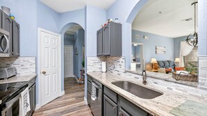 A kitchen with a marble countertop, a sink, and a stove. There is a door leading to another room. - Disney | Condo | Windsor Hills | Water Park (Kissimmee)