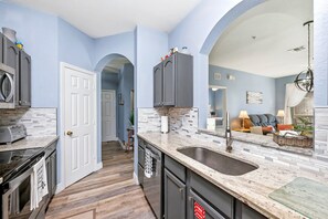 A kitchen with a marble countertop, a sink, and a stove. There is a door leading to another room.