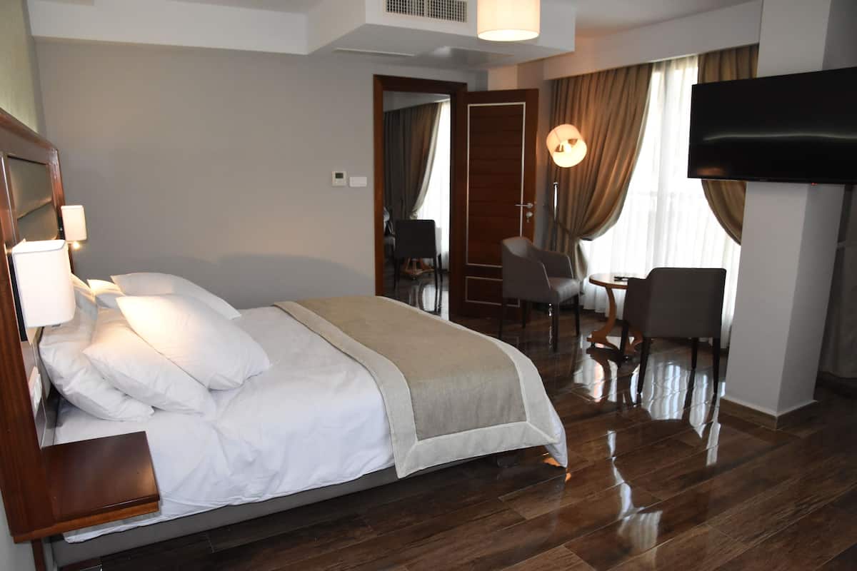 A hotel room with a bed, bedside table, lamp, TV, and a desk with a chair.