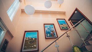 Un escalier avec une rampe en verre, trois tableaux encadrés accrochés au mur et des lampes sphériques suspendues au plafond.