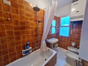 Een badkamer met een bad, wastafel en een toilet met bidetfunctie.