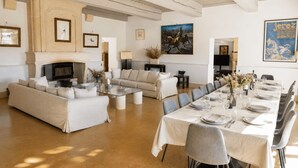 A spacious living room with a fireplace, a dining area set for six, and a modern kitchen in the background. - Mas des Bécasses in Provence 22 pax (Arles)
