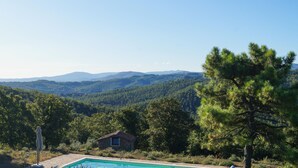 A pool area with a stone house and pine trees in the foreground, set against a backdrop of rolling hills and mountains. - 6 bedroom awesome home in Anghiari (Anghiari)