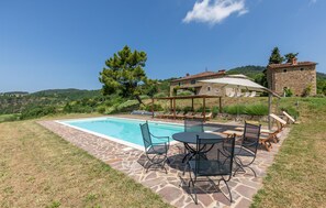 Un área de piscina con un patio de piedra, sillas de descanso y una mesa con sillas.