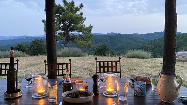 An outdoor dining setup with a table set for two, featuring candles, wine glasses, and a bowl of food. - 6 bedroom awesome home in Anghiari (Anghiari)