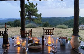 Mesa al aire libre para dos personas, con velas, copas de vino y un bol de comida.