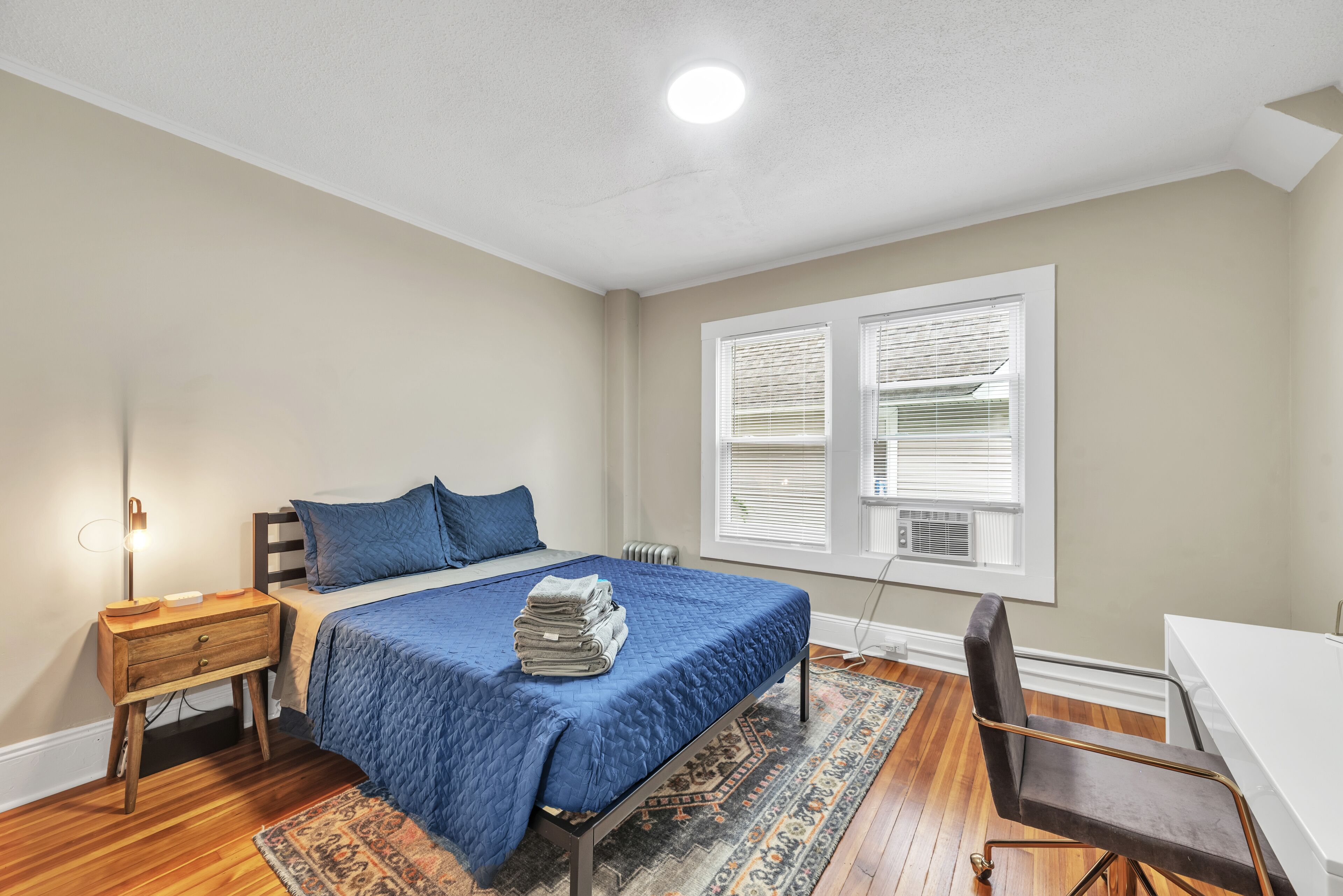 Une chambre à coucher avec un lit, une table de chevet, une chaise et une fenêtre avec des stores.