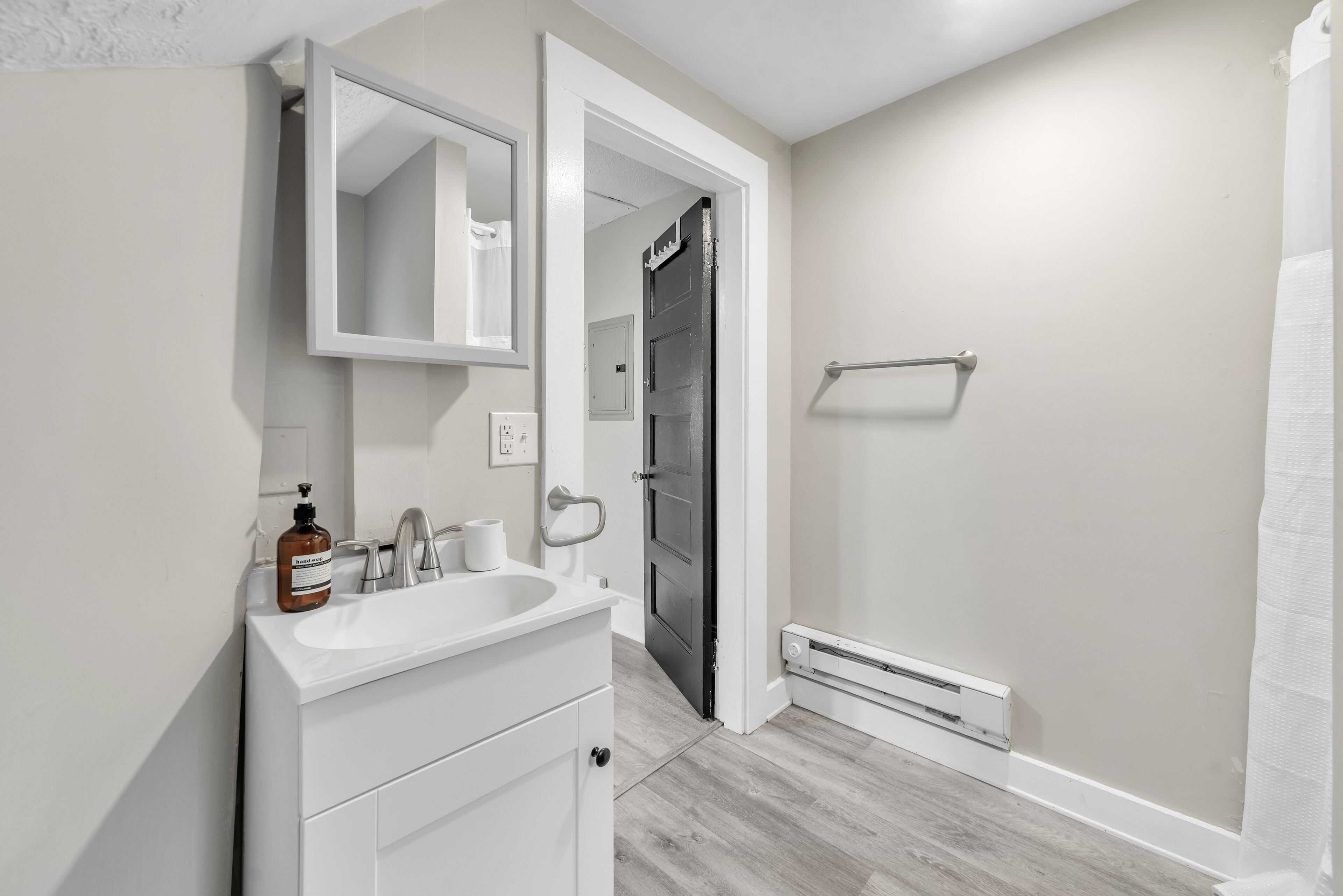 Une salle de bain avec un meuble-lavabo blanc, un miroir, un porte-serviettes et un rideau de douche.