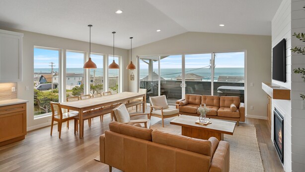 A spacious living room with a large window overlooking the ocean, a cozy seating area, and a fireplace. - Brand New Luxury Beach Home w Hot Tub & Sauna (Rockaway Beach)