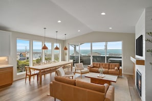 Uma sala de estar ampla com uma grande janela com vista para o oceano, um espaço de estar aconchegante e uma lareira.