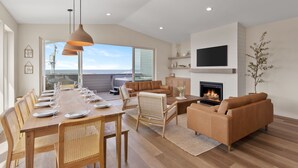 A spacious living room with a dining area, a fireplace, and a large TV mounted on the wall. - Brand New Luxury Beach Home w Hot Tub & Sauna (Rockaway Beach)