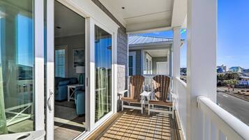 A balcony with a wooden deck, sliding glass doors leading to an interior with a sofa and a table, and a view of the street and buildings in the background.