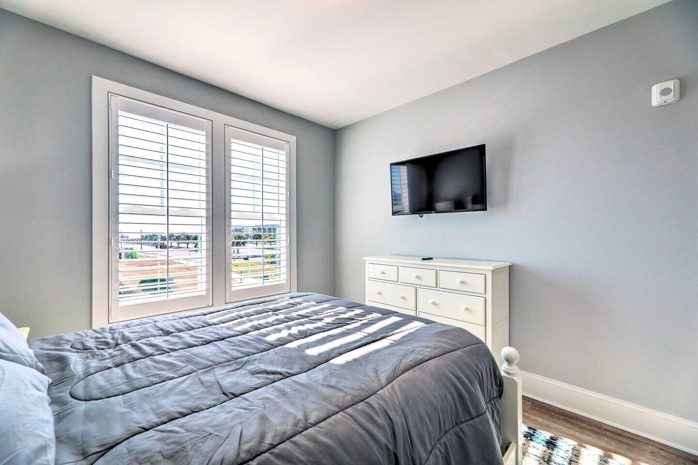 A bedroom with a bed, a dresser, a TV, and a window with blinds.