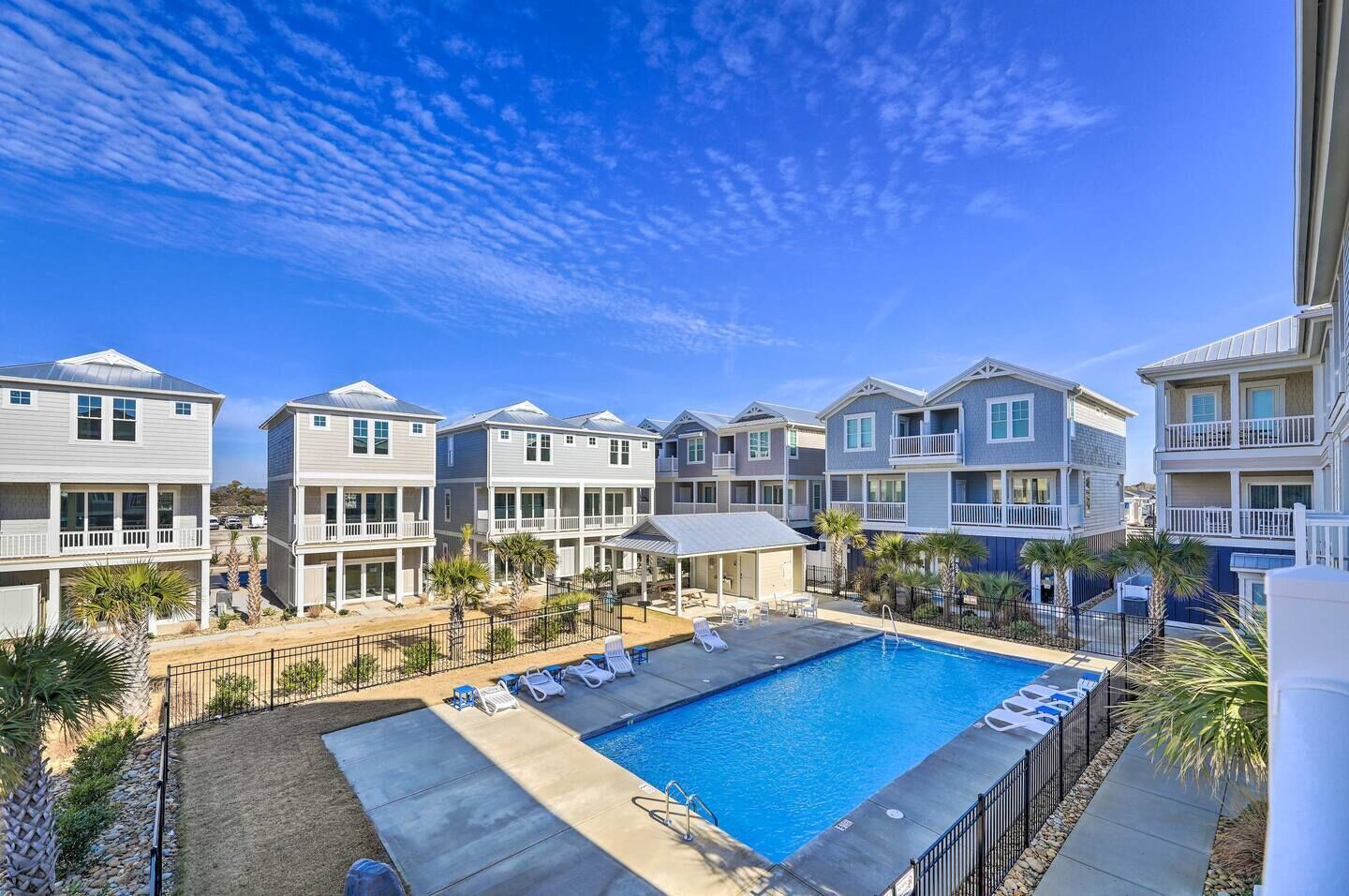 A pool area with multiple lounge chairs and a clear blue sky.