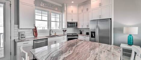 A modern kitchen with white cabinetry, a marble island, stainless steel appliances, and a large window.
