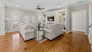 A spacious living room with hardwood flooring, two white sofas, a coffee table, and a ceiling fan. - Serene Smart Home, Big Backyard, PET FRIENDLY! (Tallahassee)